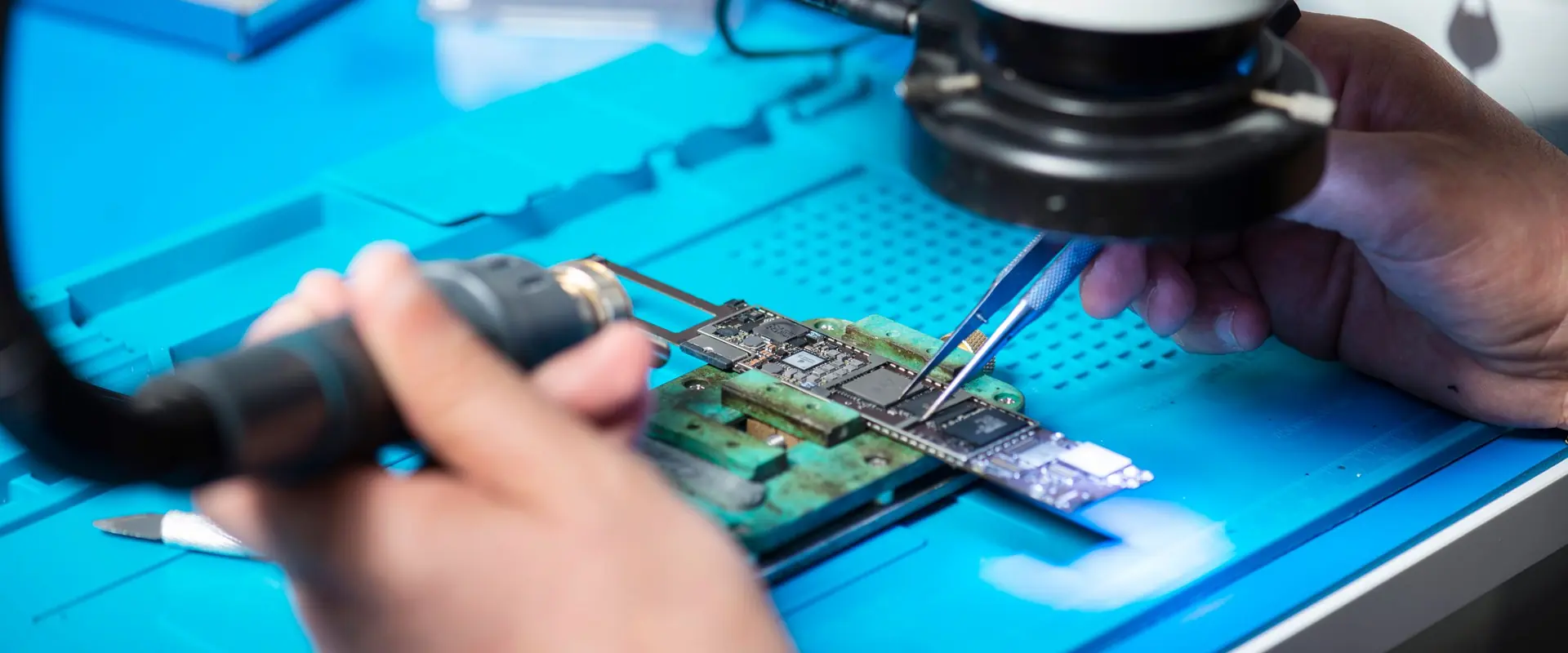 Mikroskop altında havya ve cımbızla elektronik kart onarımı yapan teknisyenin elleri